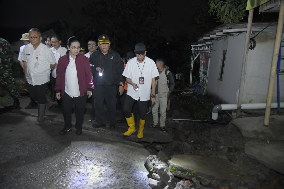 Pejabat daerah bersama petugas meninjau retakan tanah di permukiman warga pada malam hari menggunakan senter untuk memeriksa kondisi jalan yang terdampak pergerakan tanah.