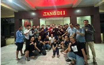 Sejumlah pria berpose bersama di depan gedung bertuliskan TANG II pada malam hari sambil mengangkat tangan dengan gestur kepalan.