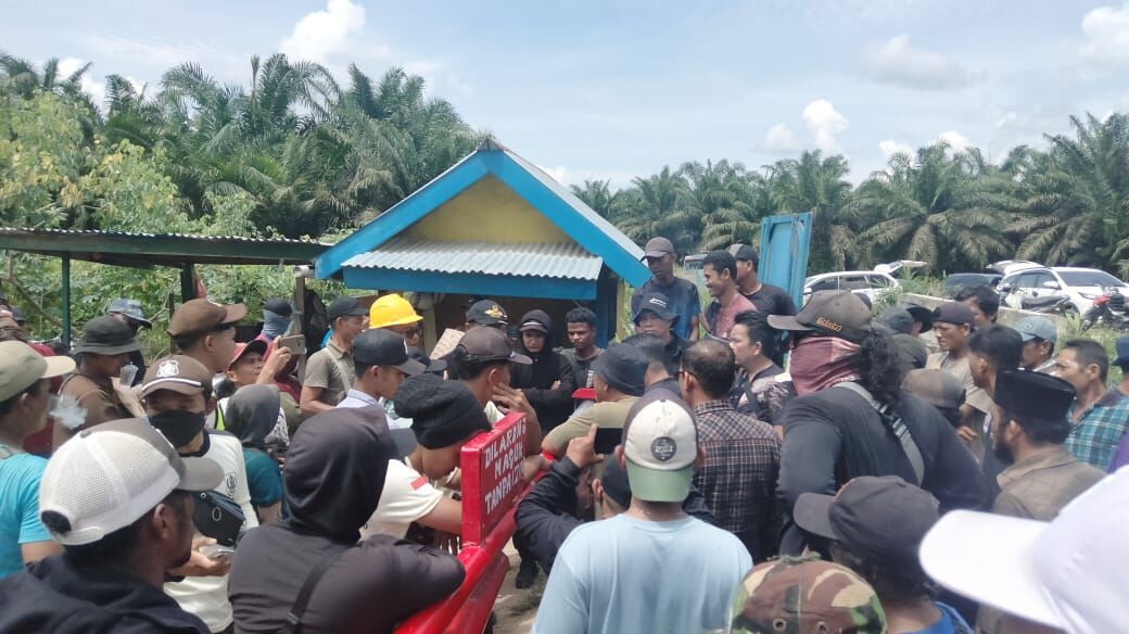 Kerumunan pekerja dan petugas pengamanan berkumpul di depan bangunan barak di area perkebunan kelapa sawit Rokan Hulu.