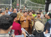 Pejabat pemerintah daerah memberikan pernyataan kepada warga dan aparat di depan gerbang kantor pemerintahan saat berlangsungnya pertemuan di area luar gedung.