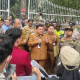 Pejabat pemerintah daerah memberikan pernyataan kepada warga dan aparat di depan gerbang kantor pemerintahan saat berlangsungnya pertemuan di area luar gedung.