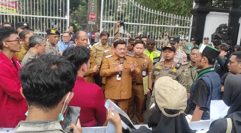 Pejabat pemerintah daerah memberikan pernyataan kepada warga dan aparat di depan gerbang kantor pemerintahan saat berlangsungnya pertemuan di area luar gedung.